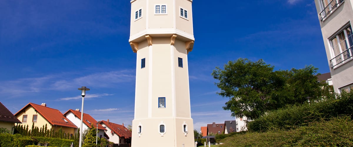 A white tower with a dome and a cross on top, surrounded by houses with red roofs and greenery.