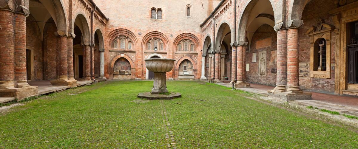 An ancient courtyard with a central fountain, surrounded by brick arches and columns.