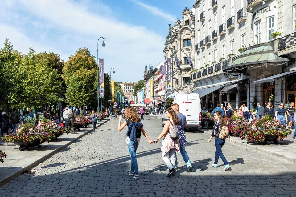 Una calle adoquinada bordeada de edificios históricos, macetas con flores y peatones.