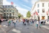 A bustling urban street with historic buildings, pedestrians, and a clear sky.