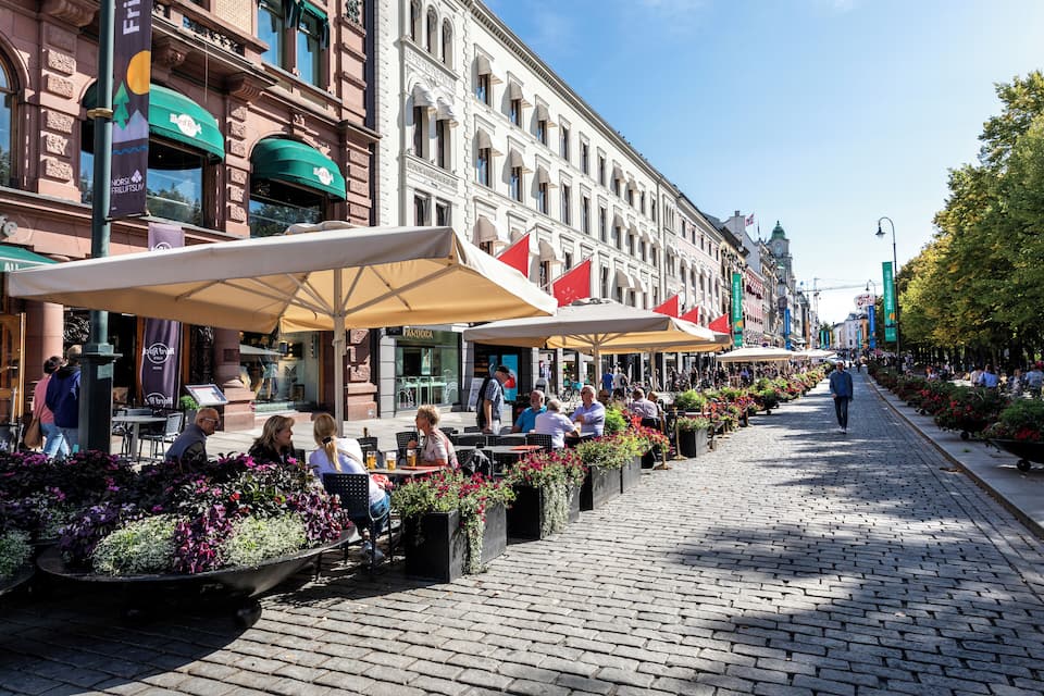 A cobblestone street lined with outdoor cafes and flower planters.