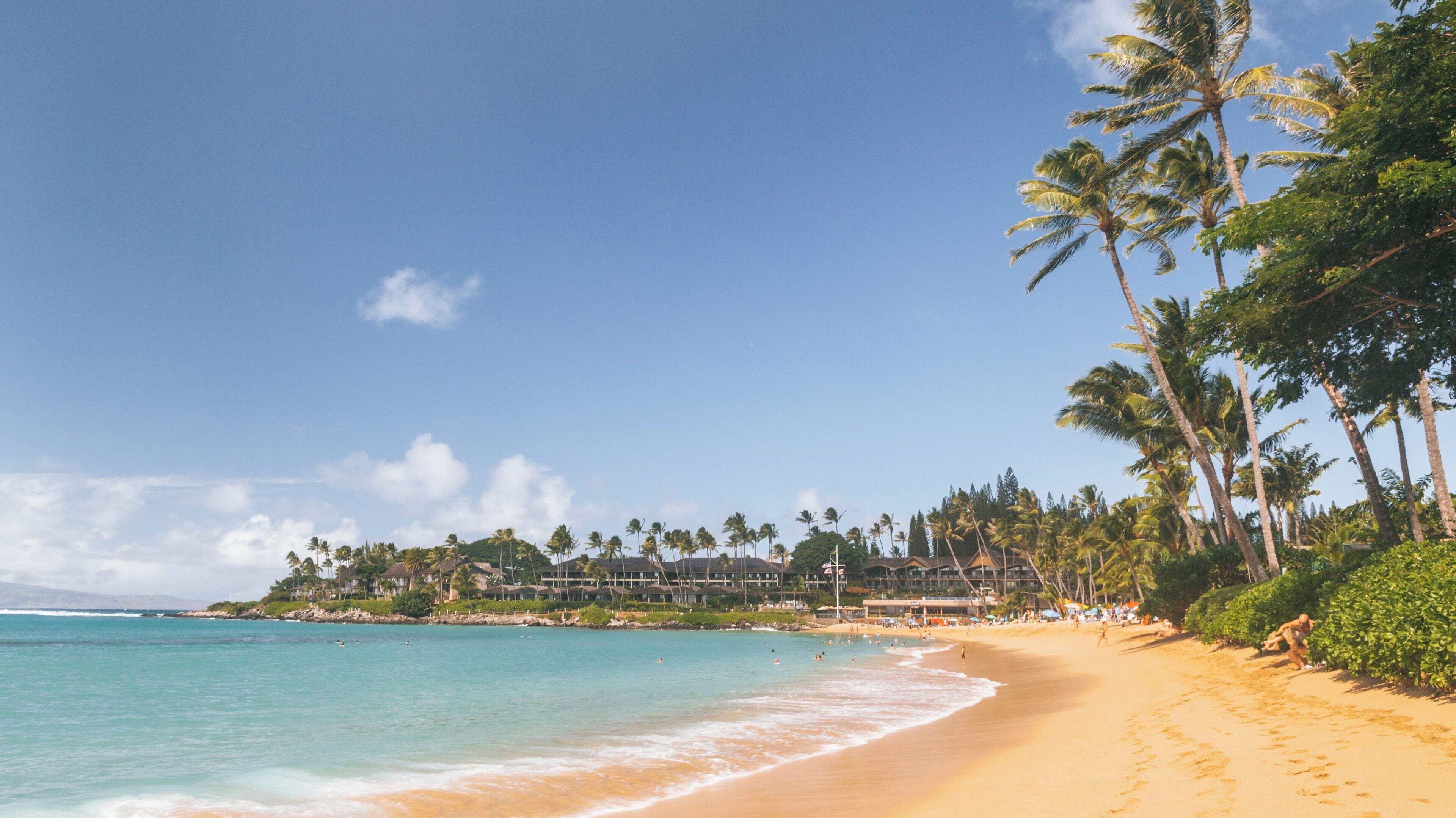 Napili Bay showcases soft golden sands and clear blue waters under a vibrant sky in Lahaina, Hawaii, perfect for sunbathing and swimming