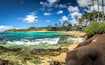 A tropical beach with clear turquoise waters, a rocky shoreline, and a resort with palm trees in the background.