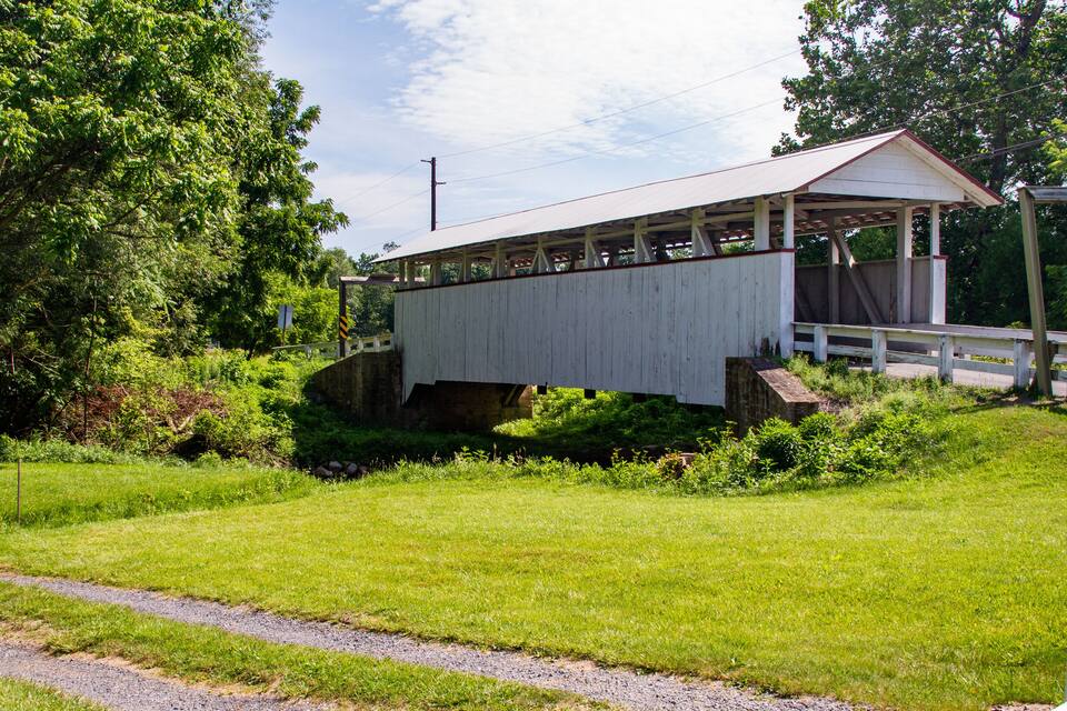 A wooden covered bridge over a small stream, surrounded by lush greenery and trees.