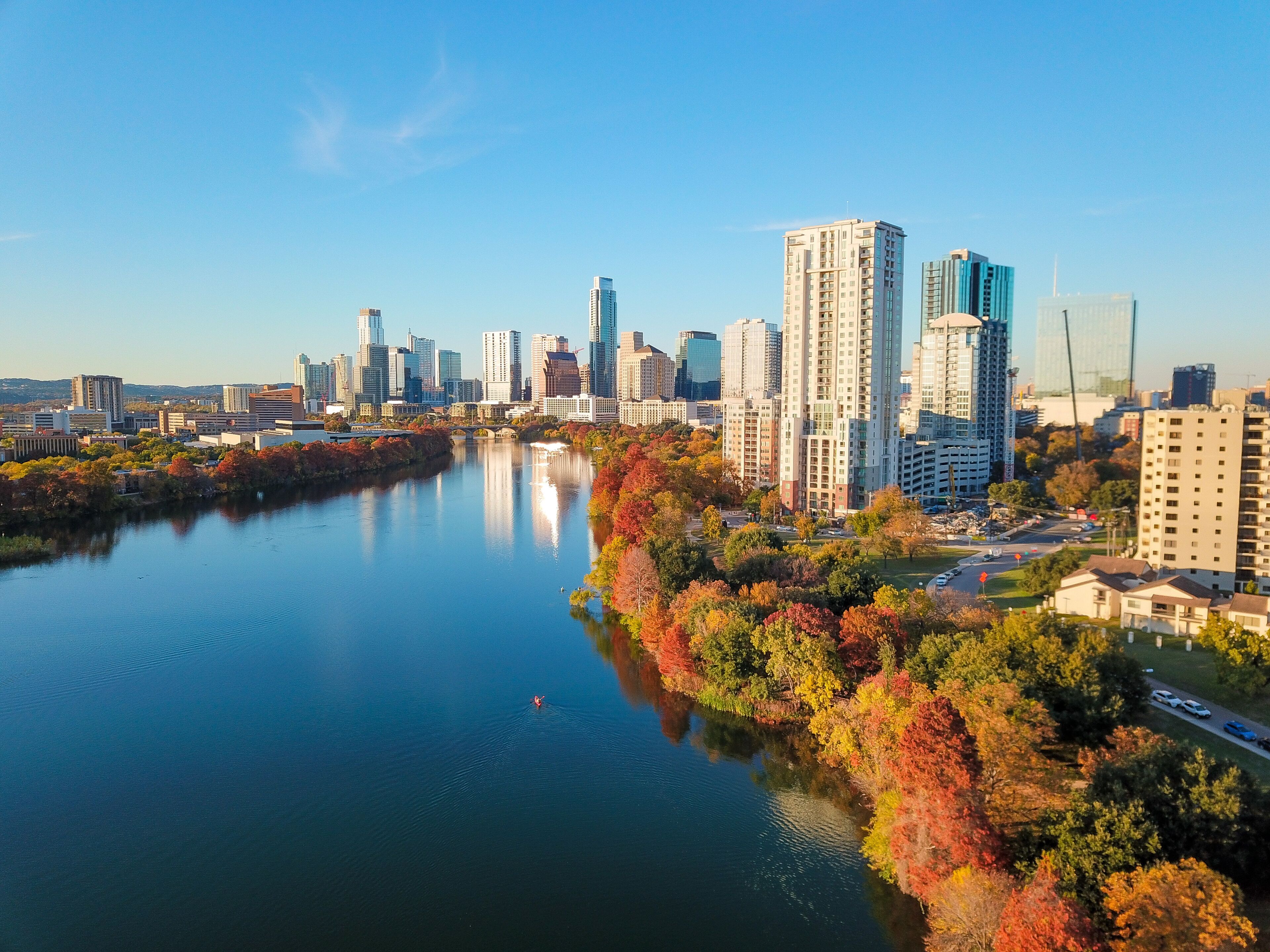 A river reflecting tall buildings, surrounded by autumn-colored trees.