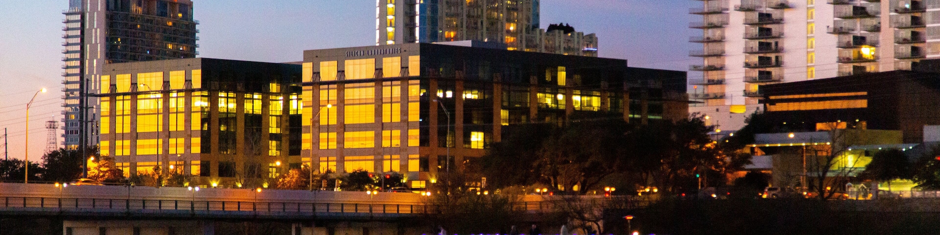 Un río con un bote, un puente y edificios iluminados al fondo.