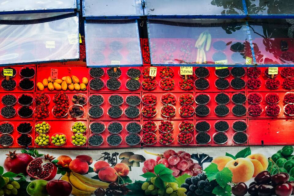 A fruit stand with various berries and fruits displayed in red bins.