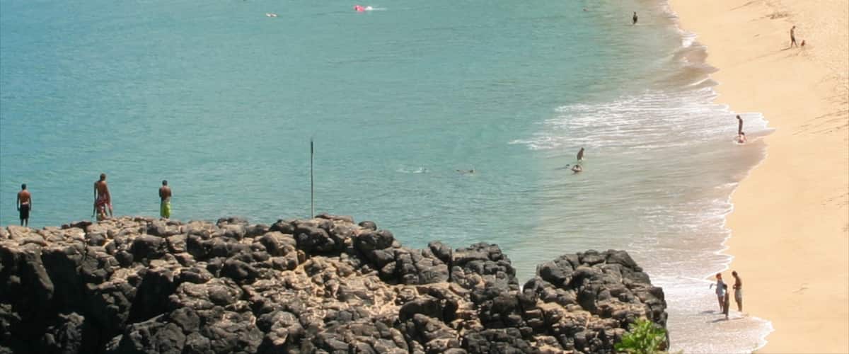 Waimea Bay featuring a sandy beach and general coastal views as well as a small group of people