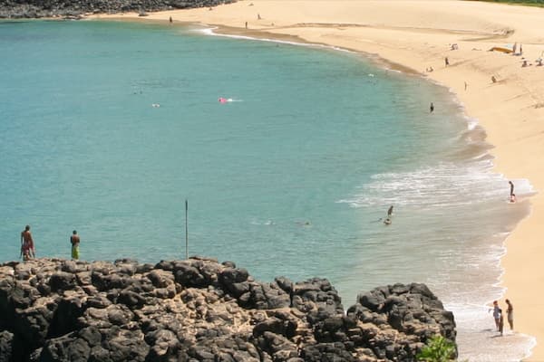 Waimea Bay featuring a sandy beach and general coastal views as well as a small group of people