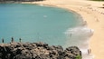 Waimea Bay featuring a sandy beach and general coastal views as well as a small group of people