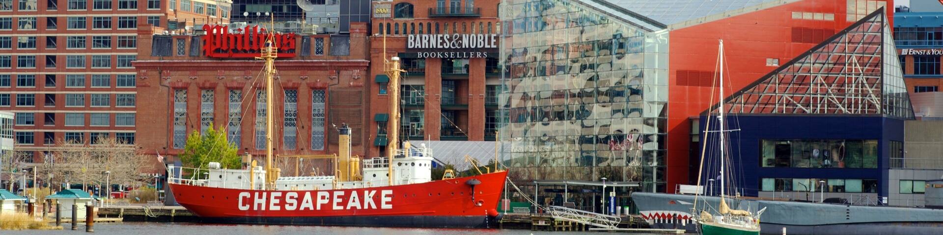 A red ship named Chesapeake docked at a port with a cityscape in the background.