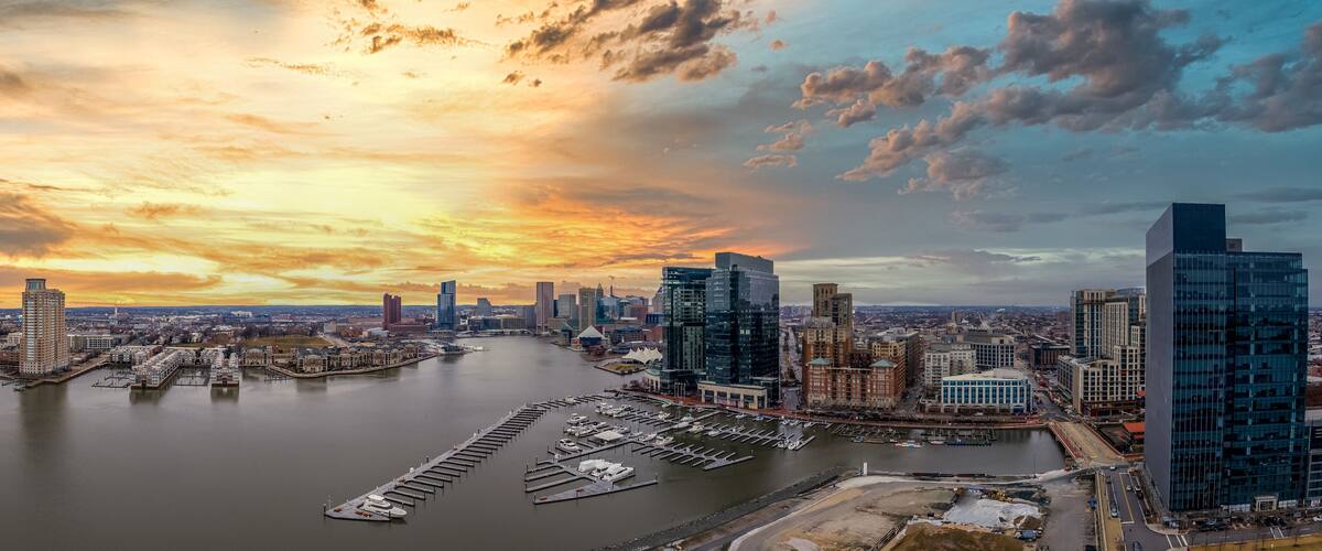 A cityscape with a river, marina, and modern buildings during sunset.