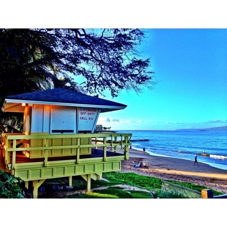 A lifeguard station with a sign that reads "Lifeguard Duty Call 911" on a beach with the ocean in the background.