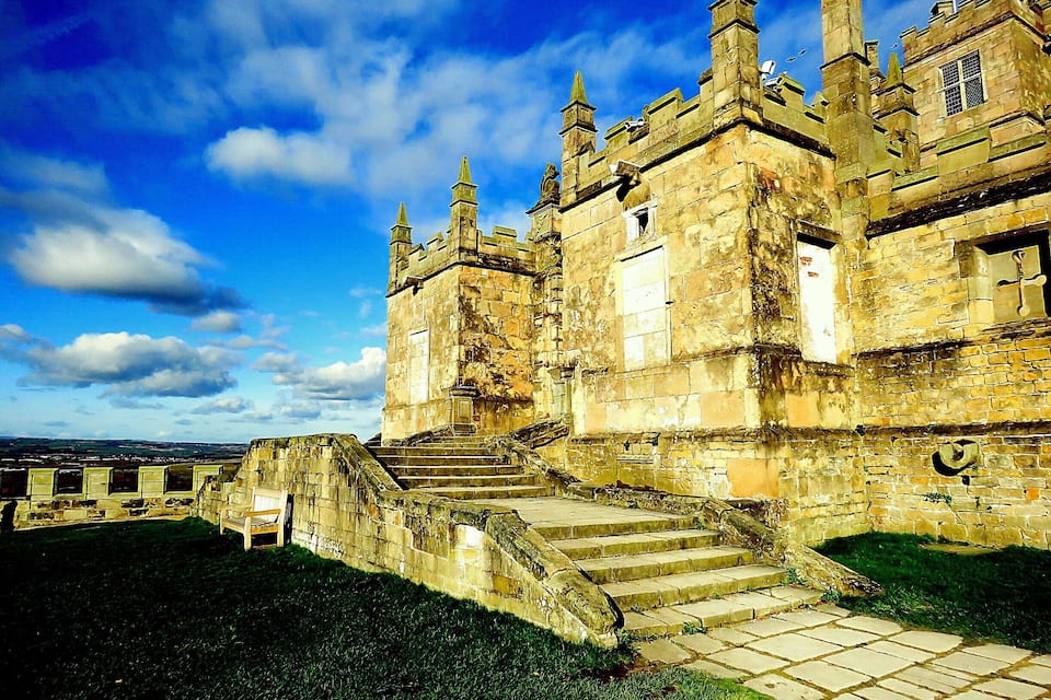 A historic castle with stone walls, multiple towers, and a set of stone steps leading up to the entrance.