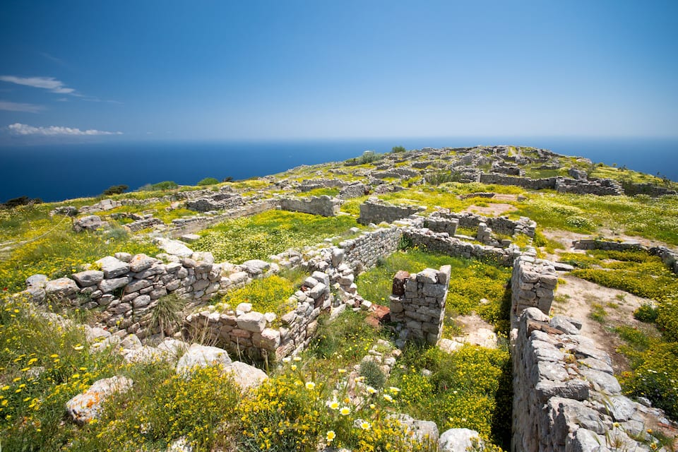 Ancient stone ruins on a hillside with a clear view of the sea.
