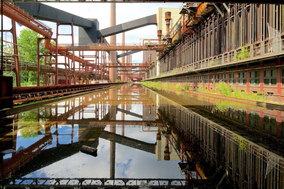 An industrial area with a canal reflecting structures and greenery.