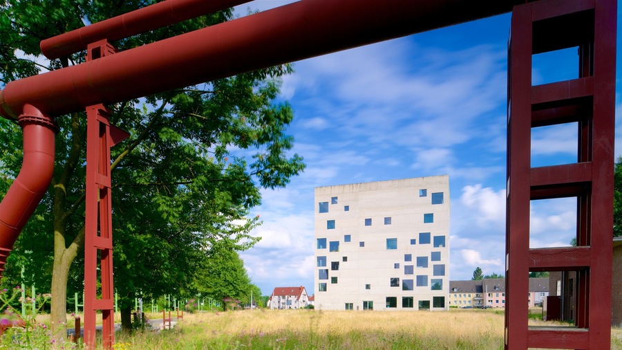 Un edificio moderno con una facciata originale, circondato da alberi verdi rigogliosi e un cielo azzurro limpido.