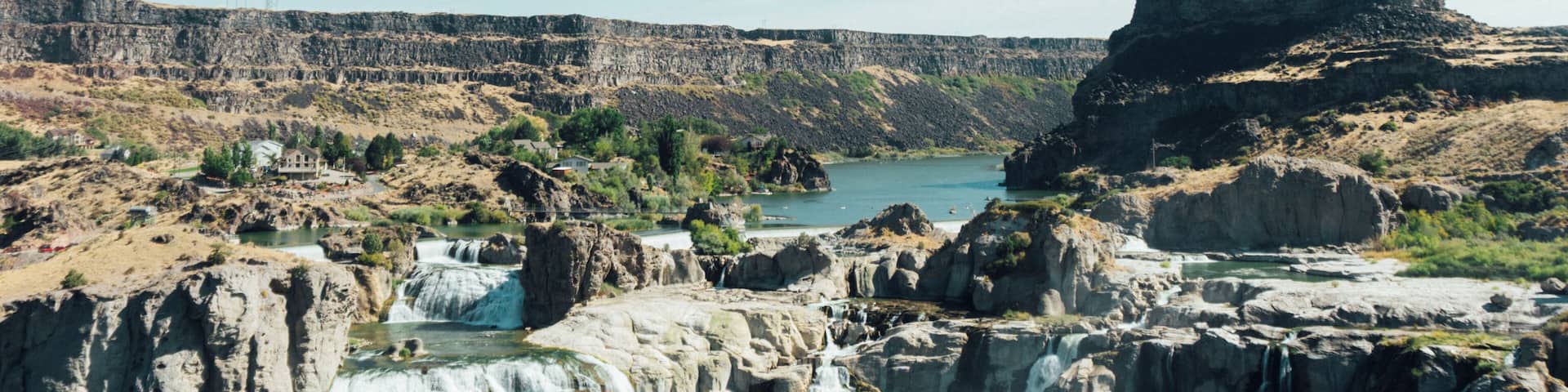 A waterfall cascading into a river surrounded by rocky cliffs and a small building on the left.