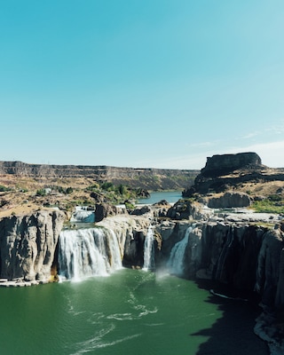 A waterfall cascading into a river surrounded by rocky cliffs and a small building on the left.