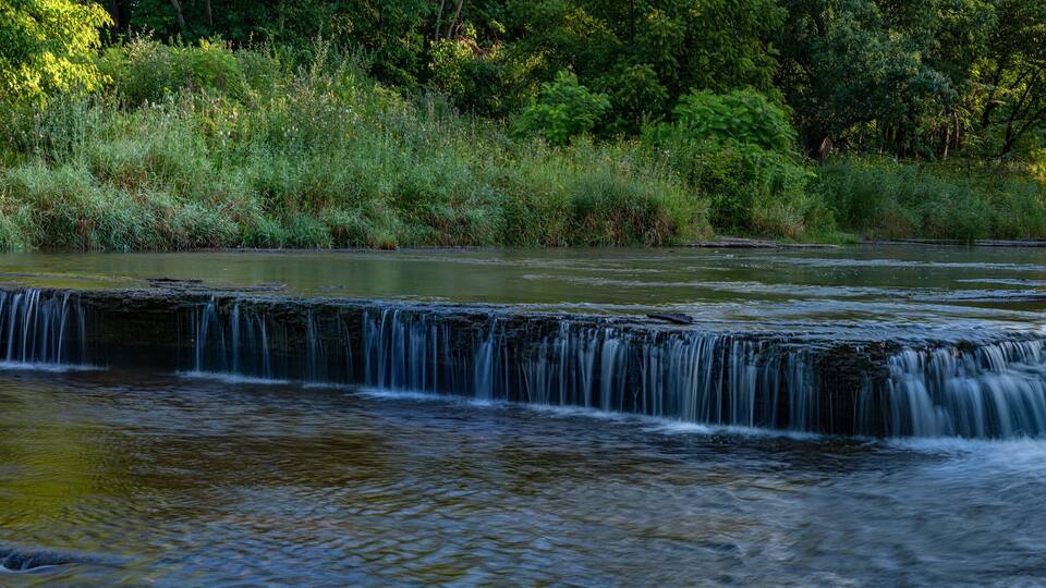 A waterfall cascading over a rocky ledge surrounded by lush greenery.
