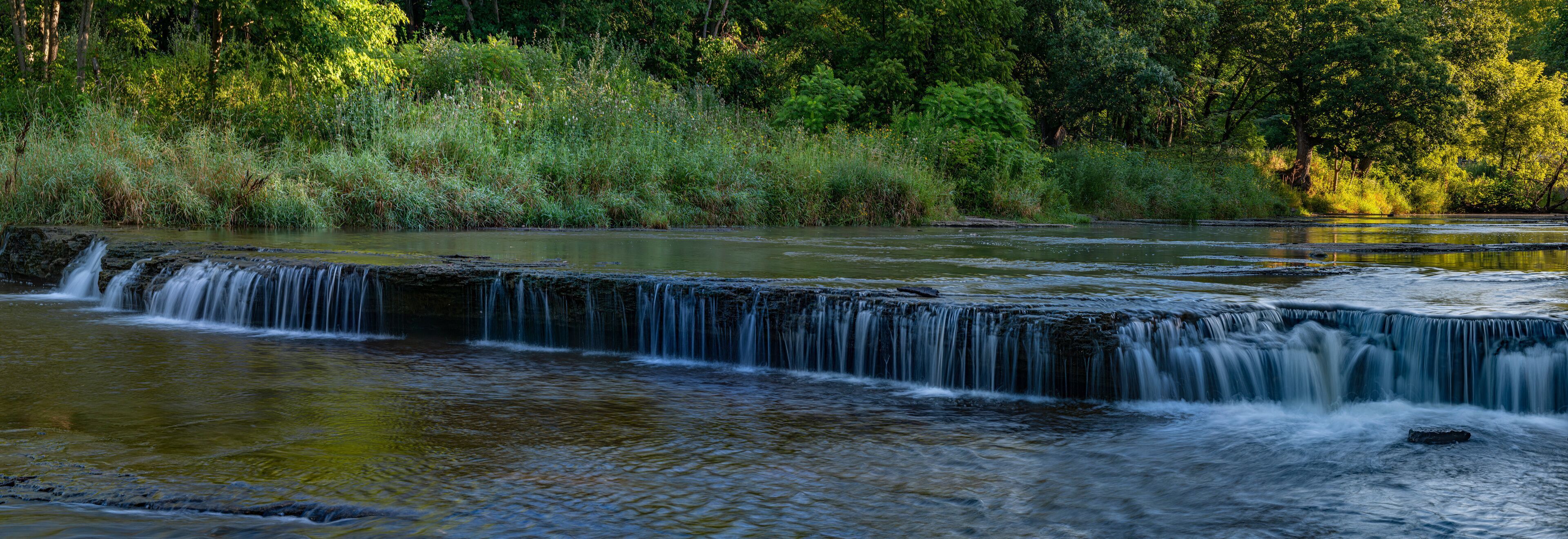 A waterfall cascading over a rocky ledge surrounded by lush greenery.