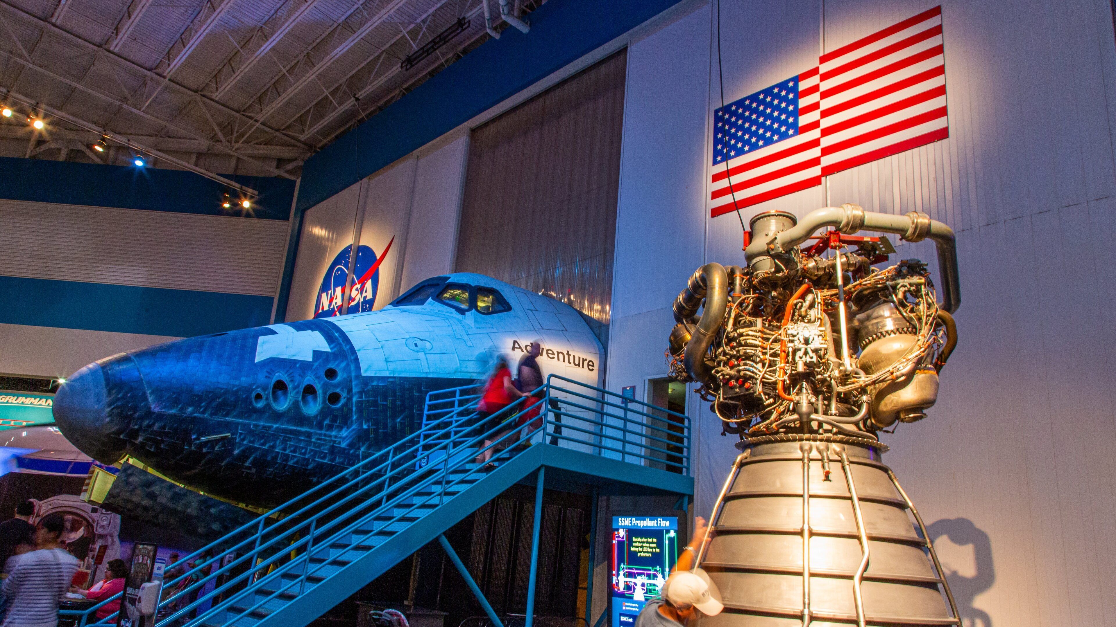 A space shuttle on display with an American flag and a large engine model.