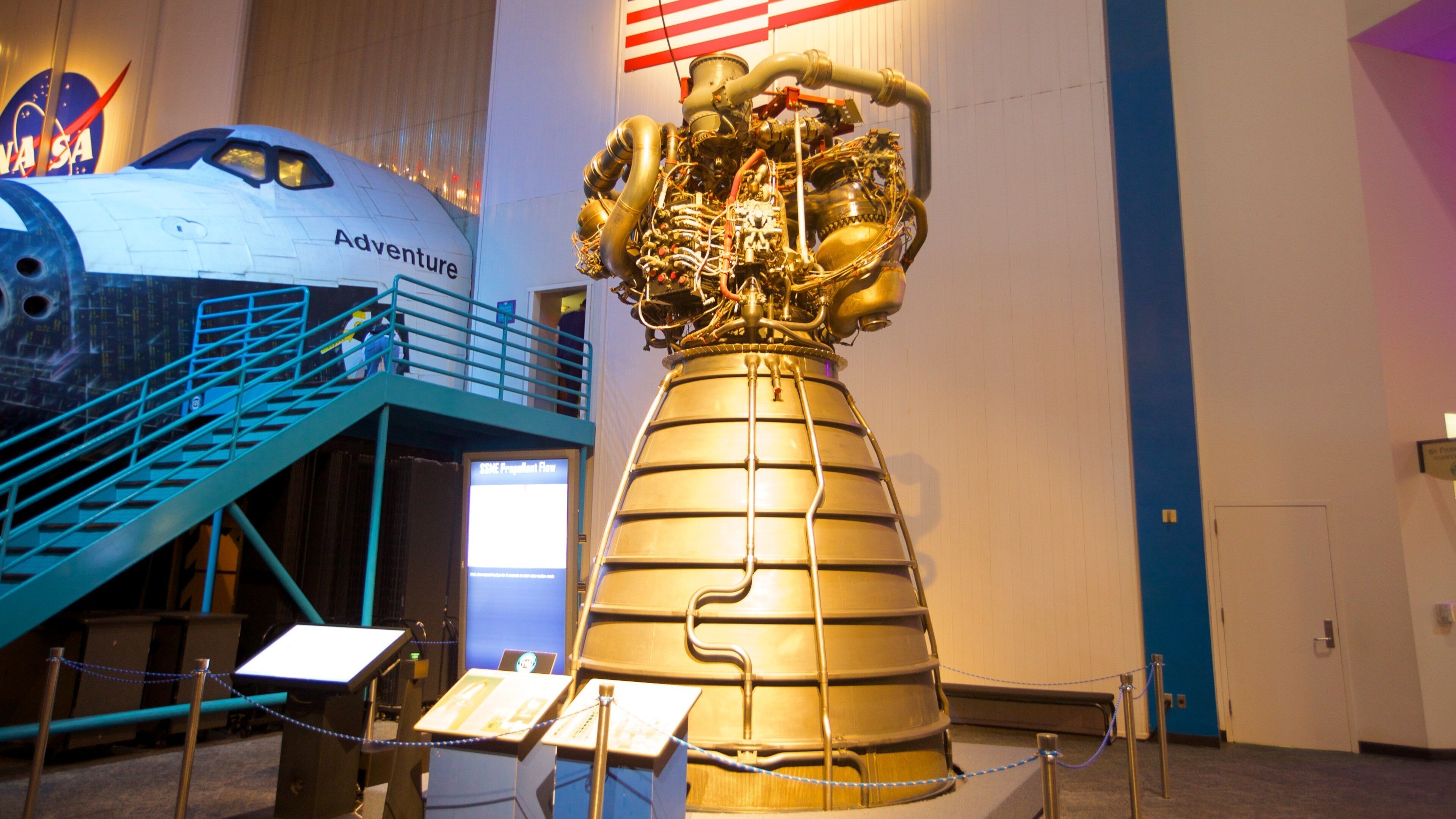 A space shuttle on display with a large rocket engine model in front.