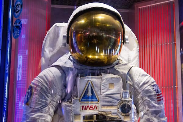 Un astronauta in tuta spaziale con il logo NASA e l'emblema di uno space shuttle.