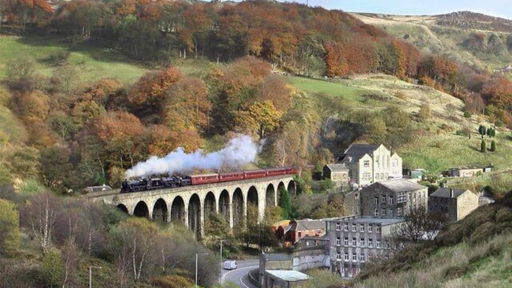 A train on a viaduct, a village with stone buildings, and autumn-colored trees.