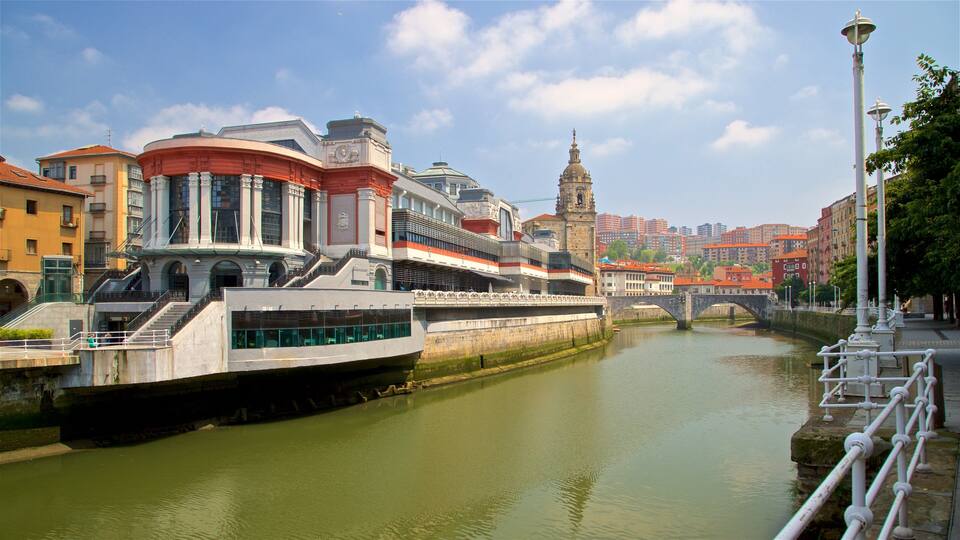 Un río con un puente, edificios y una torre al fondo.
