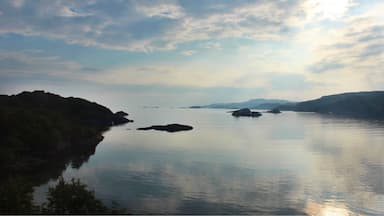 A calm lake with rocky outcrops and distant mountains under a partly cloudy sky.