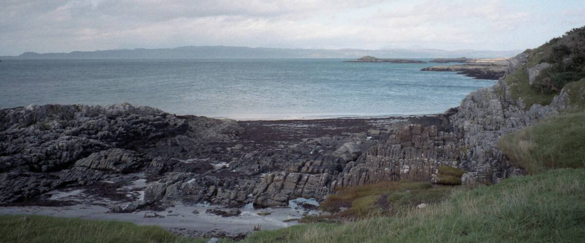 A rocky coastline with calm sea and distant mountains.