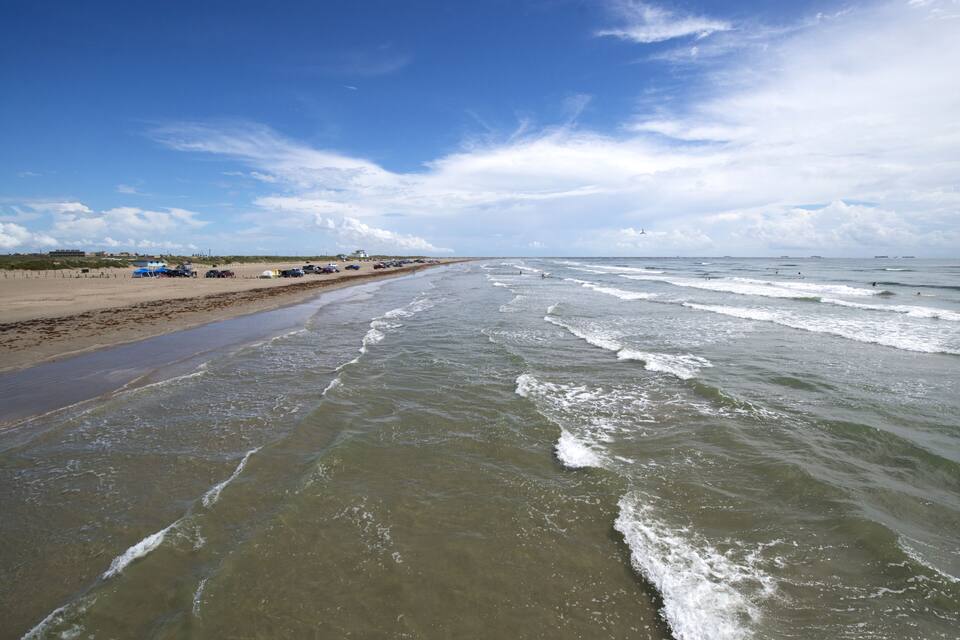 A beach with waves, a clear sky, and a distant ship.