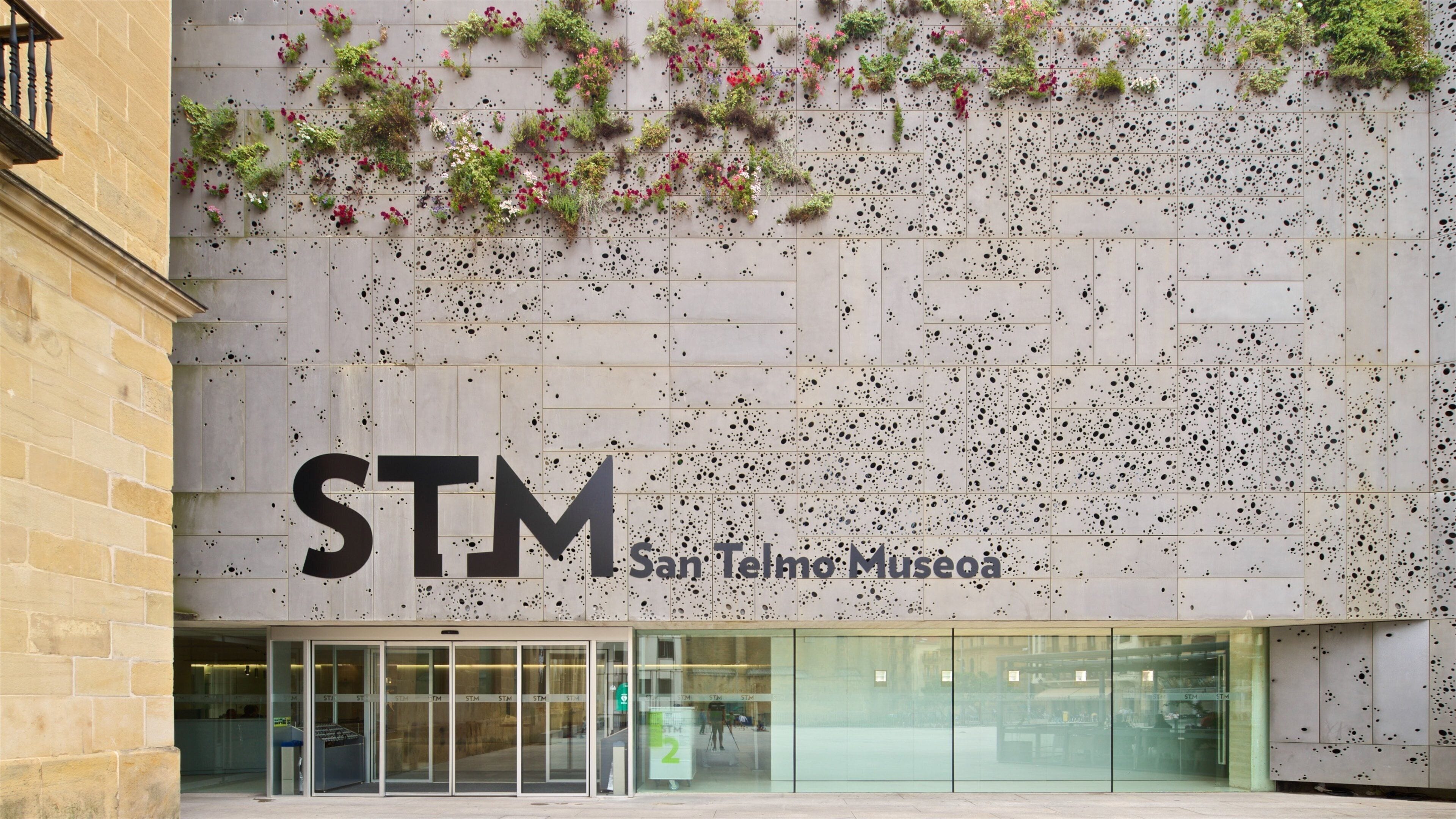 Das äußere Erscheinungsbild des San Telmo Museums mit einem großen 'STM'-Schild und einer mit Pflanzen und schwarzen Flecken verzierten Wand.