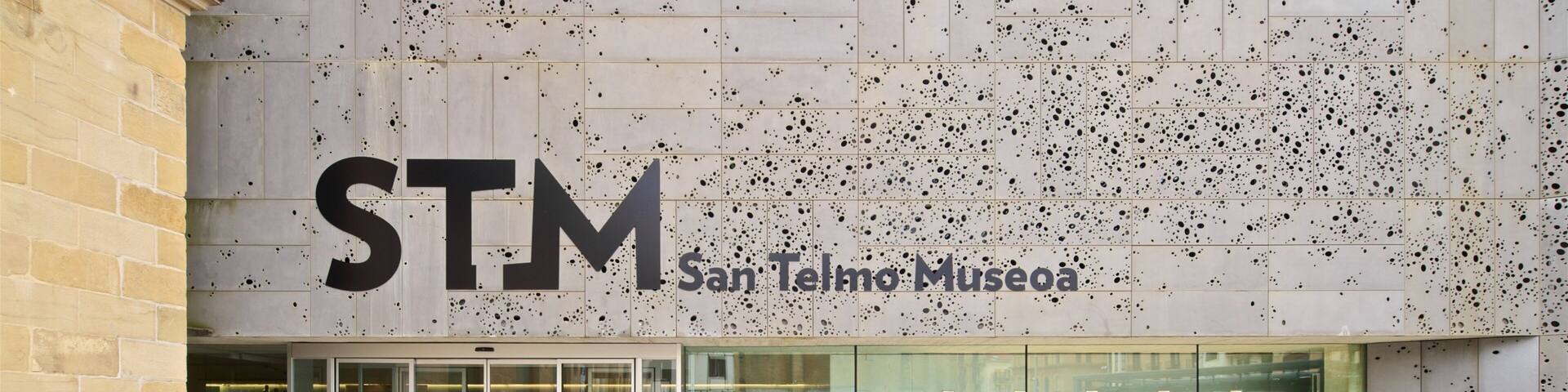 The exterior of the San Telmo Museum with a large 'STM' sign and a wall decorated with plants and black spots.