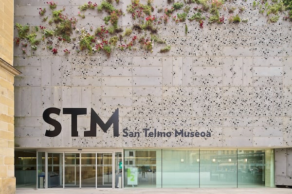 The exterior of the San Telmo Museum with a large 'STM' sign and a wall decorated with plants and black spots.