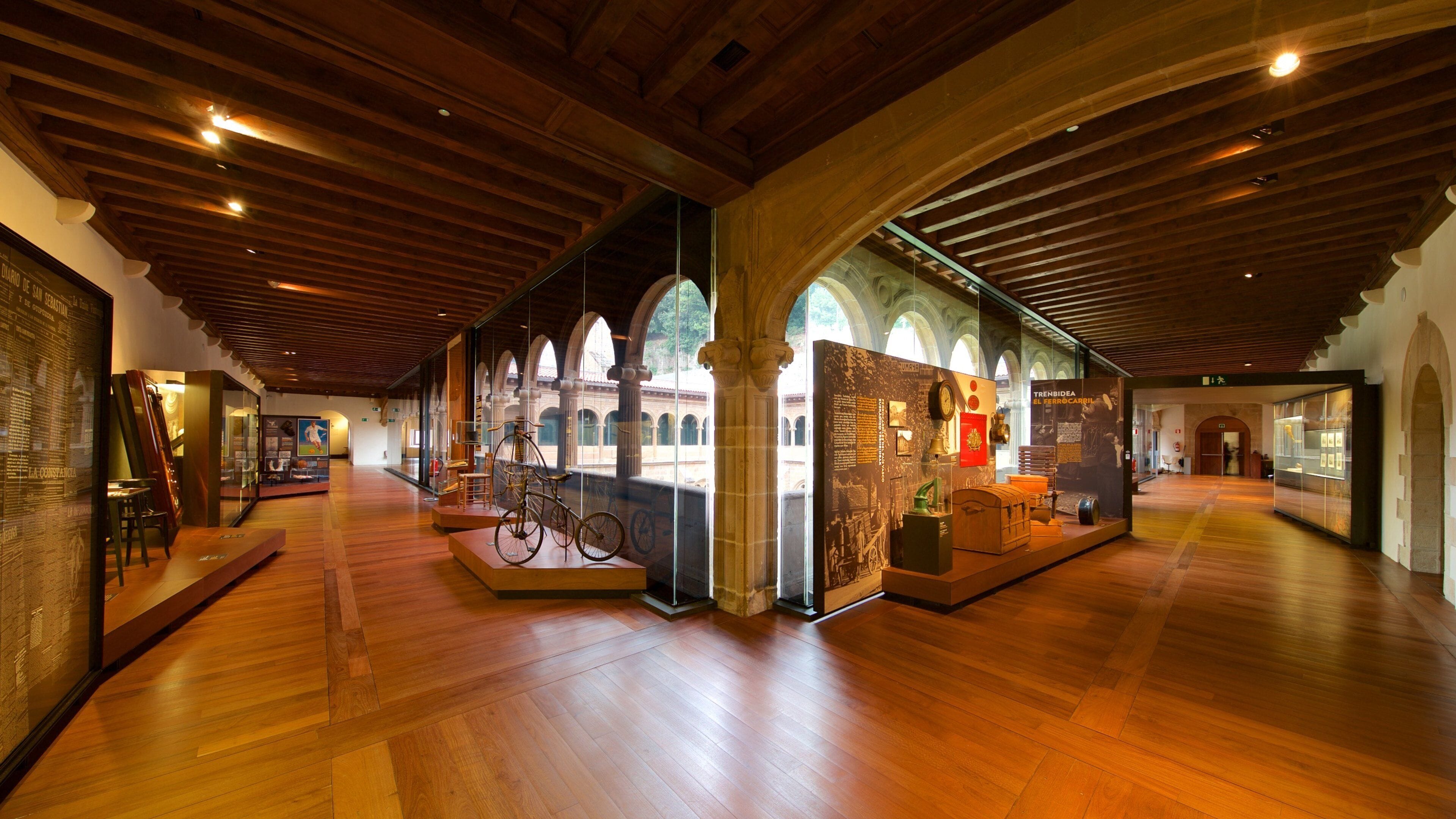 Interior de museo con pisos de madera, vitrinas de vidrio y artefactos históricos.