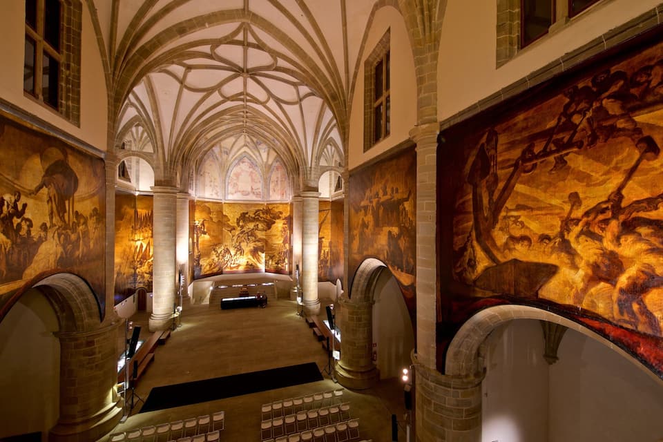 Een kathedraalinterieur met gotische architectuur, hoge gewelfde plafonds en gedetailleerde fresco's op de muren.