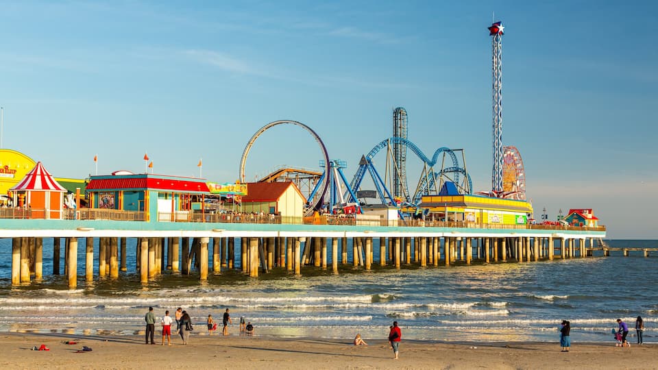 A pier with amusement rides, a Ferris wheel, and a tall observation tower by the beach.