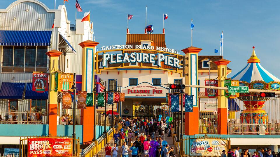 The Pleasure Pier entrance with flags, signs, and a crowd of people.