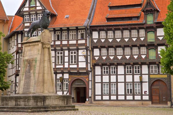 Ein traditionelles Fachwerkhäuschen mit einer auf einem Sockel stehenden Bärenstatue davor.
