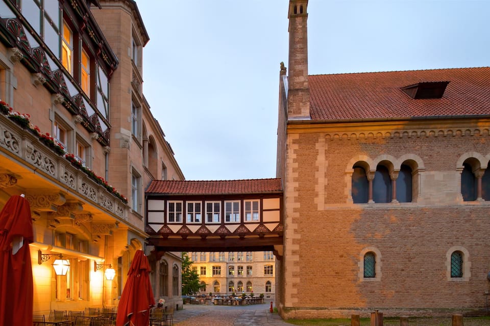 Ruas de pedra com arquitetura europeia tradicional, incluindo um edifício com estrutura de madeira e um prédio de tijolos com janelas em arco.