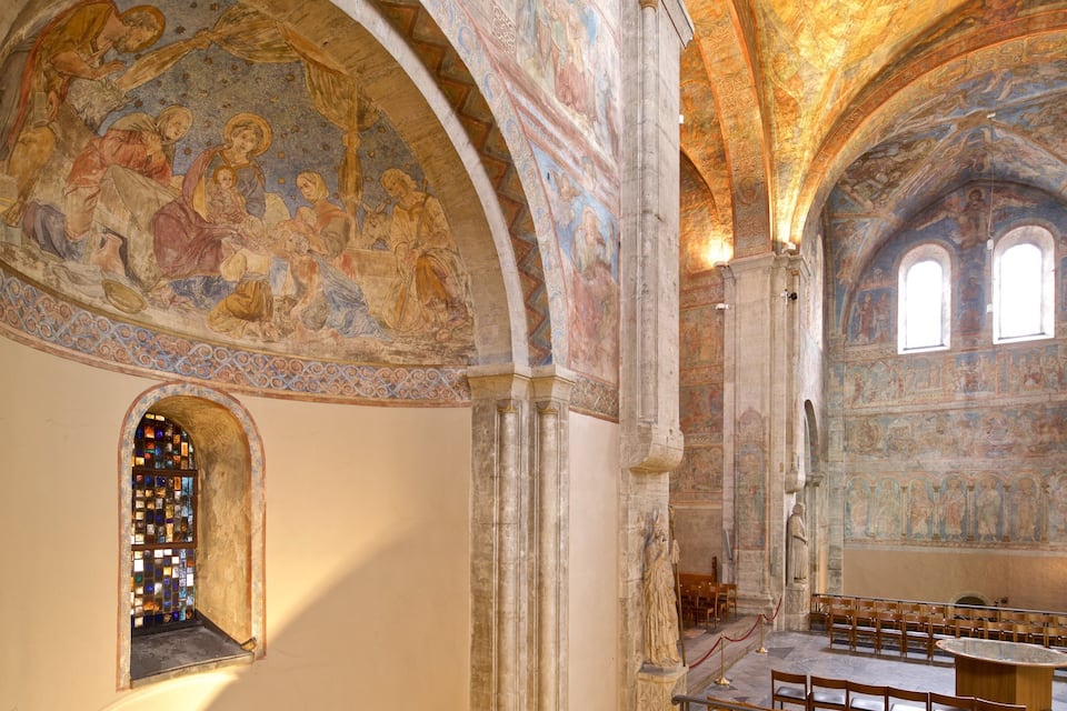 Interior de una iglesia con techo abovedado alto, vidrieras y frescos detallados.