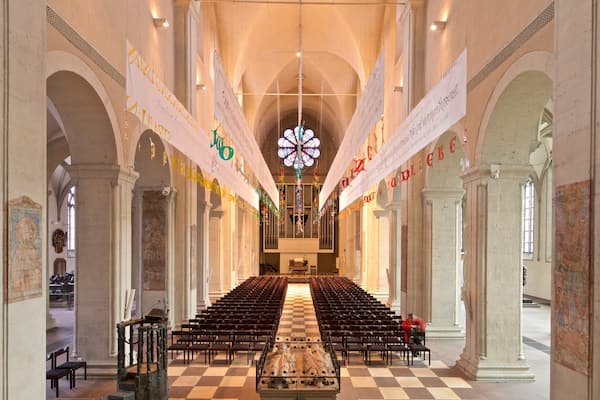 Ein Kircheninneres mit Reihen von Kirchenbänken, einem großen Buntglasfenster und Wimpeln, die von der Decke hängen.