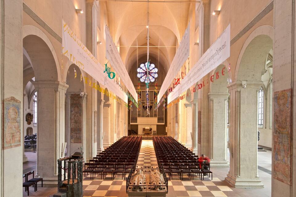 Ein Kircheninneres mit Reihen von Kirchenbänken, einem großen Buntglasfenster und Wimpeln, die von der Decke hängen.