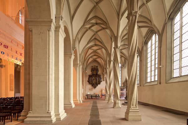 Ein Kathedraleninneres mit hohen Gewölbedecken, Reihen von Kirchenbänken und großen Buntglasfenstern.