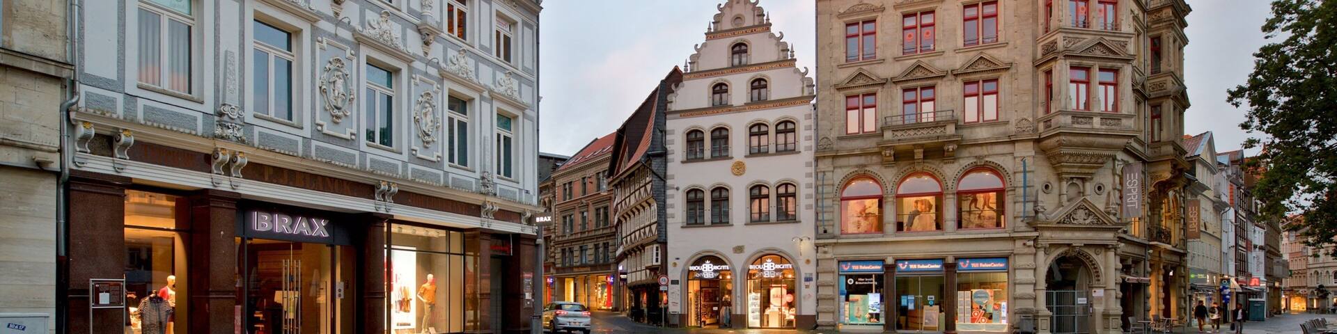 A historic European square with ornate buildings, a cobblestone street, and storefronts.