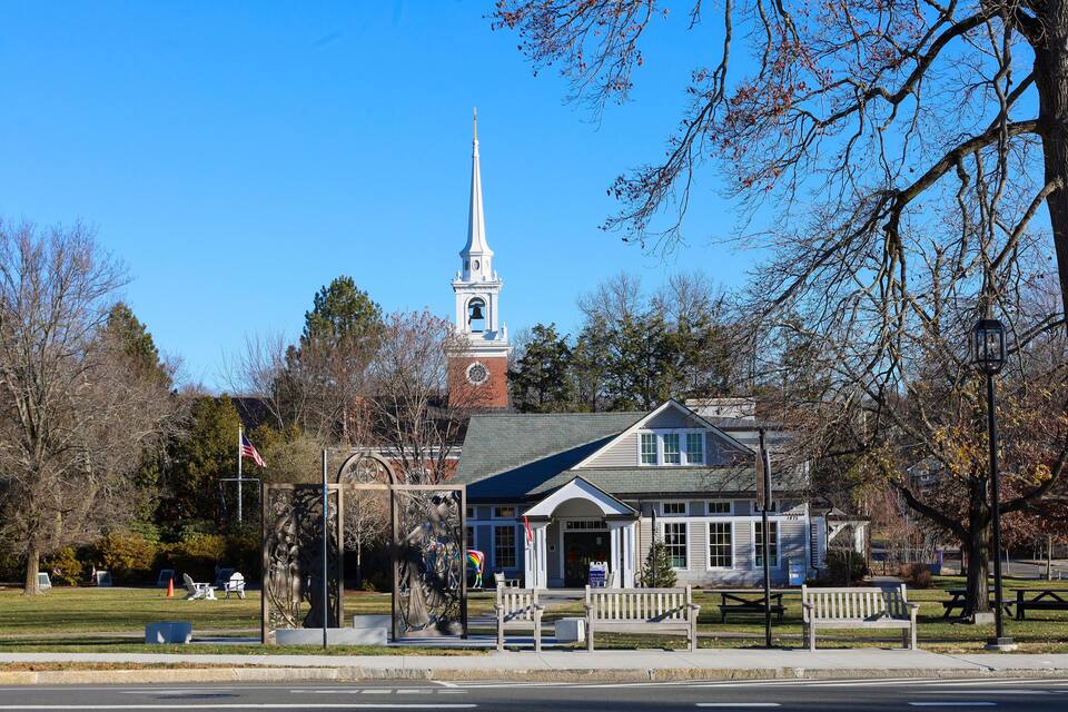 A church with a steeple, a statue, benches, and a picnic table in a park.