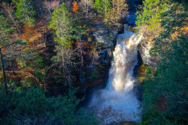 Ein Wasserfall, umgeben von Herbstlaub und einer Holzbrücke.