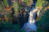 A waterfall surrounded by autumn foliage and a wooden bridge.